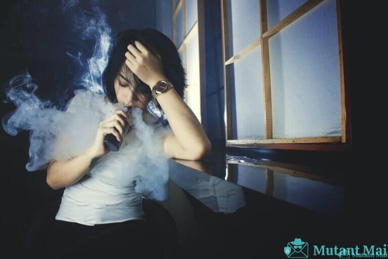 Cool casual brunette in white t shirt smoking electronic cigarette while leaning on hand in dark studio